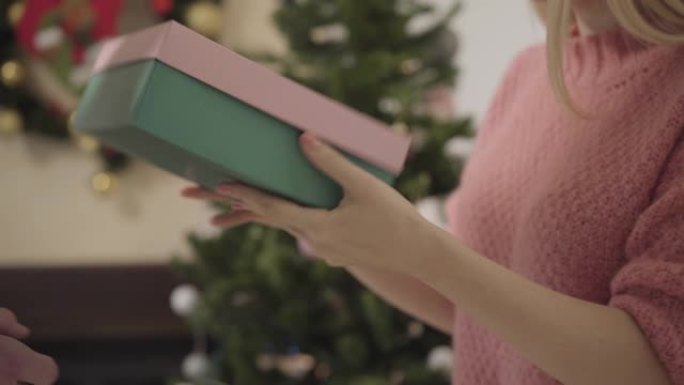 女性高加索人的特写镜头在圣诞树前拿起礼品盒，打开并扔回去。女孩对配偶的新年礼物不满意。关系问题，愤怒