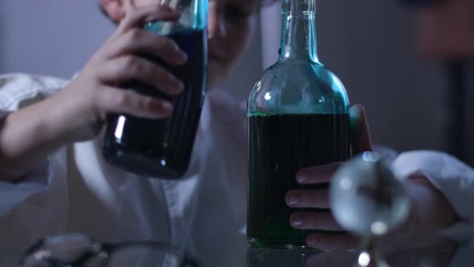 高加索男孩混合的烧瓶中的液体特写。卷发少年，穿着实验室外套，拿着装满多色化学试剂的烧瓶。智力，化学。