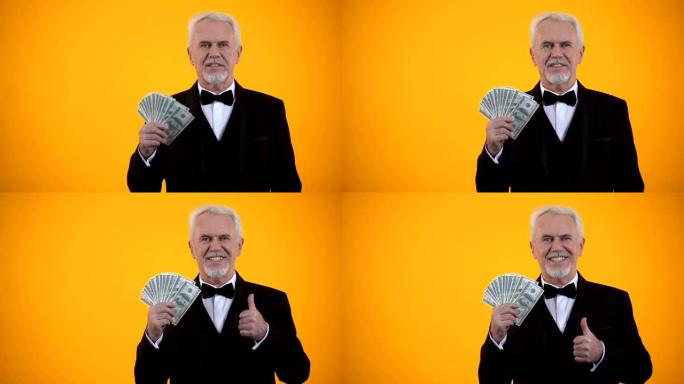 穿着西装的快乐老人拿着美元并竖起大拇指，营业收入