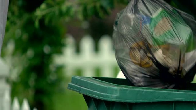 男子在绿色塑料容器中扔垃圾袋，废物利用，生态