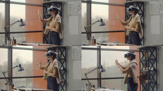 现代女性工程师-设计师在办公室的大窗户站在虚拟现实头盔中使用手势来管理项目，而无需离开办公室。施工控