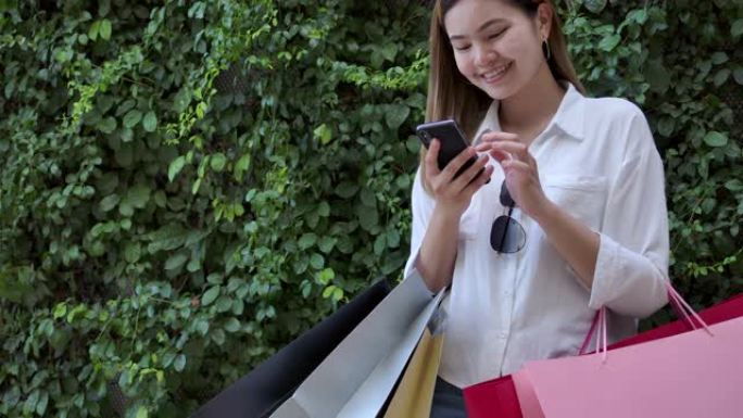 4k镜头慢动作美女走到商场外面她正在用手机，提着购物袋是五颜六色的，她很开心。买了她喜欢的东西