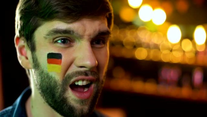 不高兴的男人脸上画着德国国旗做捂脸，球队输了比赛