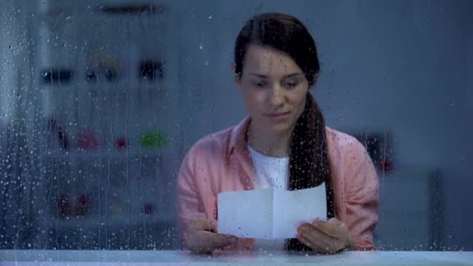 体贴的女人在下雨的窗户后面读信，怀旧的回忆