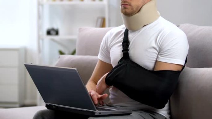 手臂吊带和颈圈的男人在家中笔记本电脑上工作，创伤治疗