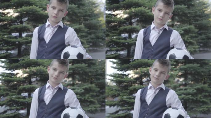 肖像可爱的衣冠楚楚的男孩站在街上拿着足球和钱包。