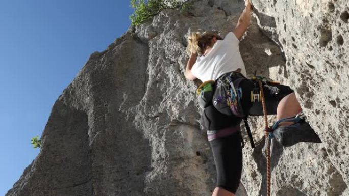 年轻女子爬上垂直的岩石面，同时带领