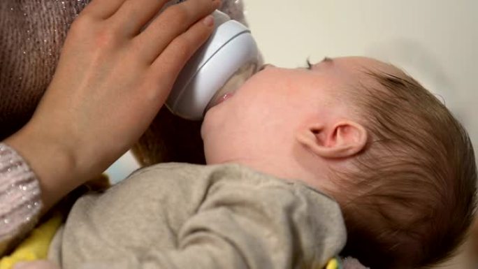 可爱的婴儿从奶瓶中吸奶配方奶粉，妈妈手上有正畸binky