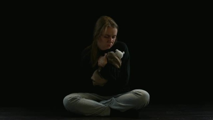 郁闷的女士坐在黑暗中拥抱泰迪熊，产科暴力受害者