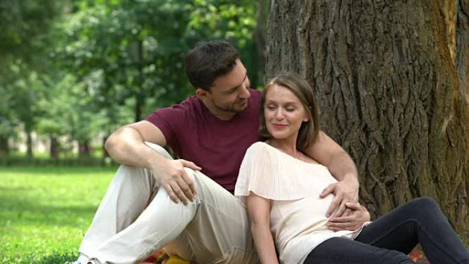 幸福的怀孕夫妇坐在公园里，计划安全的家庭生活，福利