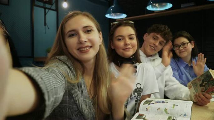 三个朋友自拍，对着相机挥手致意，坐在咖啡馆里拿着书和笔记