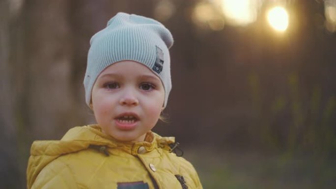 一个微笑的小男孩的特写肖像，戴着大睫毛，戴着帽子，穿着黄色外套，直接看着相机。高加索男孩2岁