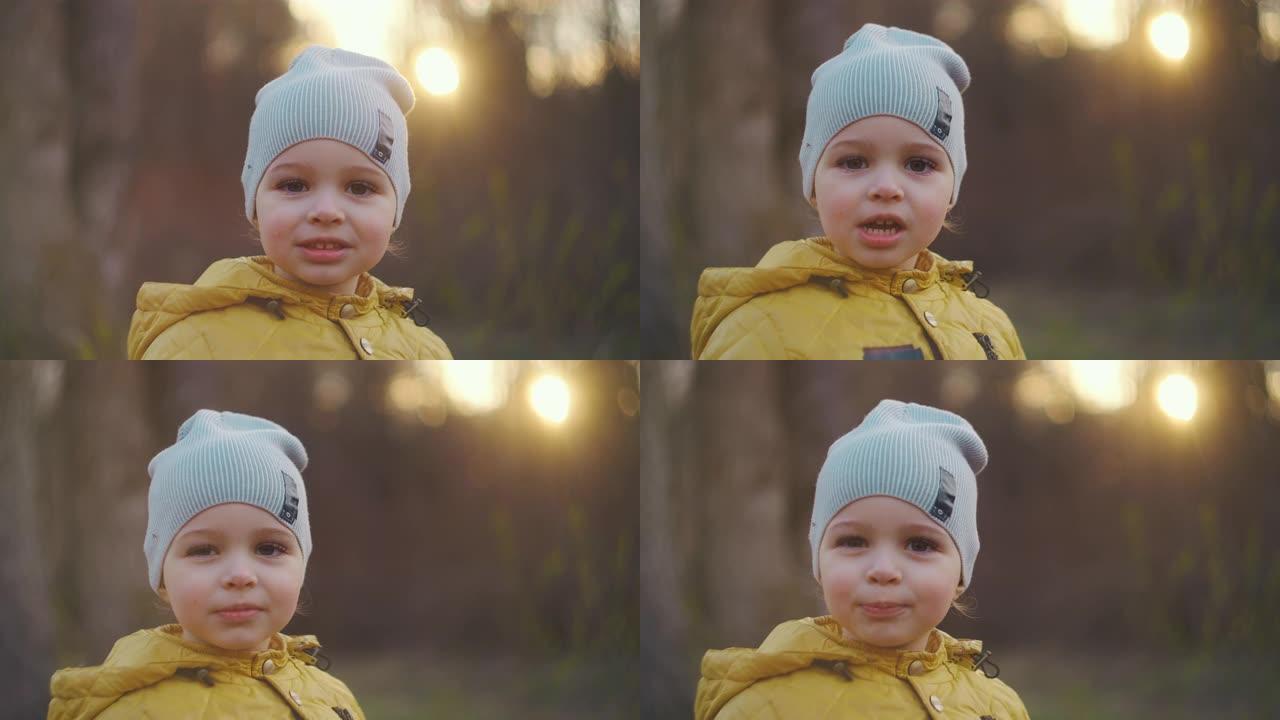 一个微笑的小男孩的特写肖像，戴着大睫毛，戴着帽子，穿着黄色外套，直接看着相机。高加索男孩2岁