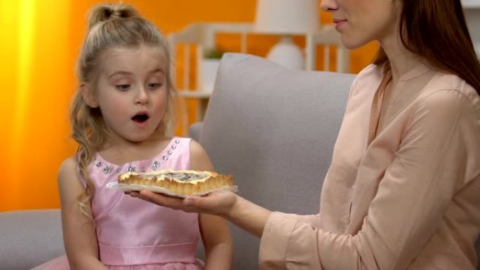 年轻的妈妈给惊讶的小女孩穿公主裙甜蛋糕，庆祝