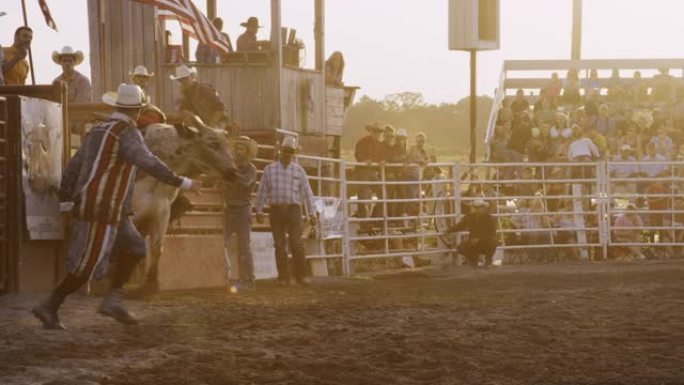 一名男公牛骑手参加公牛比赛的慢动作镜头，然后在日落时分被人从体育场的公牛背上扔出