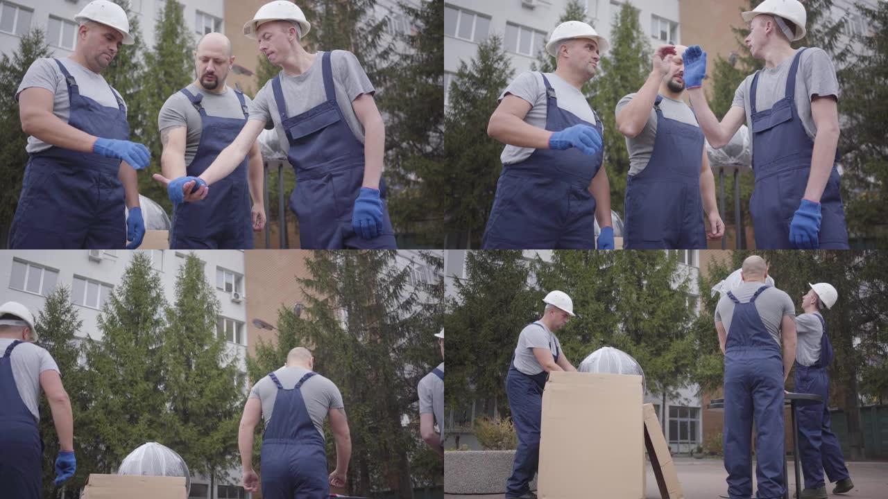 三个肌肉发达的高加索人互相把手放在一起，开始工作。穿着蓝色制服的工人拿着包裹去大楼，主管填写文件。摄
