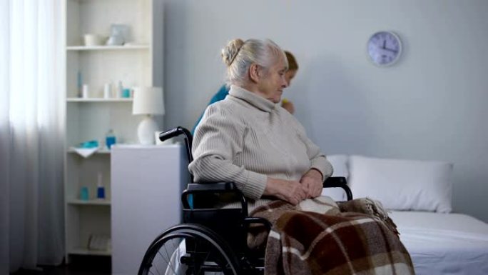 悲伤的女人坐在轮椅上看医院看门人清洁室，医疗中心