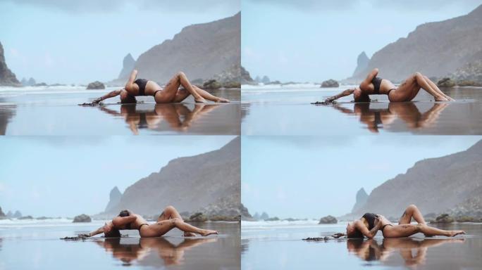 女人在海洋附近的沙滩上对着山脉和黑沙移动，在沙滩上跳舞