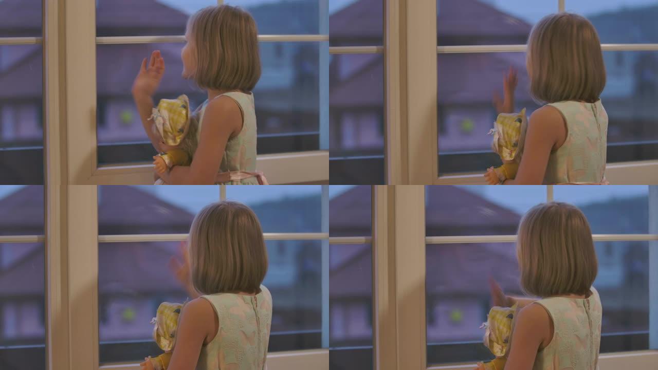 快乐的高加索小女孩抱着洋娃娃，向窗外挥手。晚上送走客人或亲戚的孩子。穿着漂亮衣服的优雅孩子呆在家里。