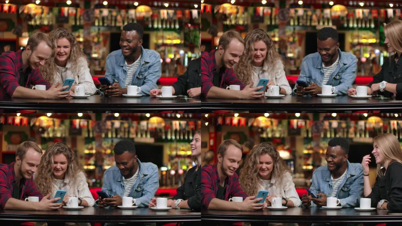 坐在咖啡馆里的四个朋友笑着看着手机屏幕，交换旅行中的照片。非裔美国女友聊天喝咖啡。