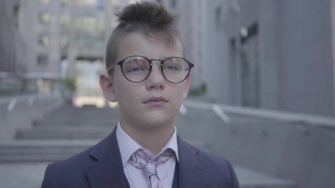肖像英俊的戴眼镜的男孩站在街上看着镜头。