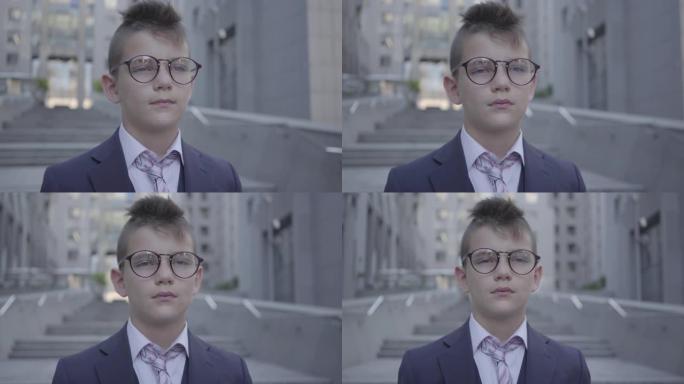 肖像英俊的戴眼镜的男孩站在街上看着镜头。