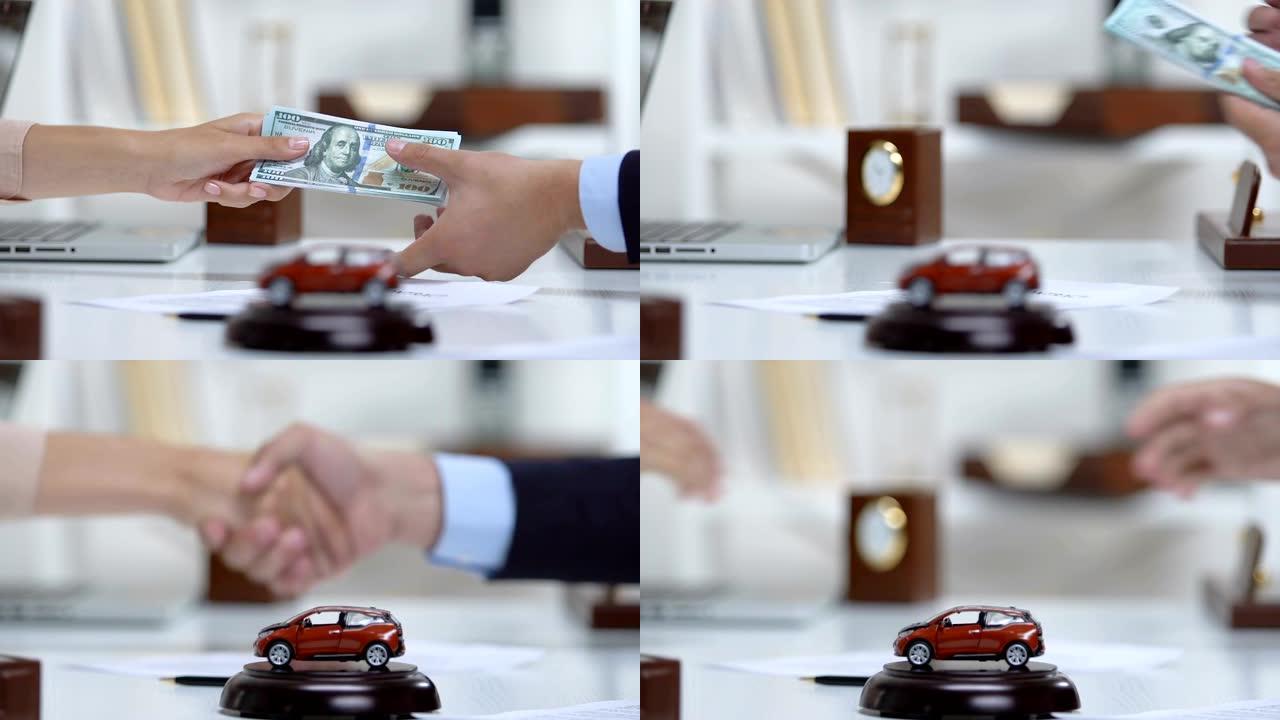 女买主给汽车商人美元，握手，桌上放着汽车玩具