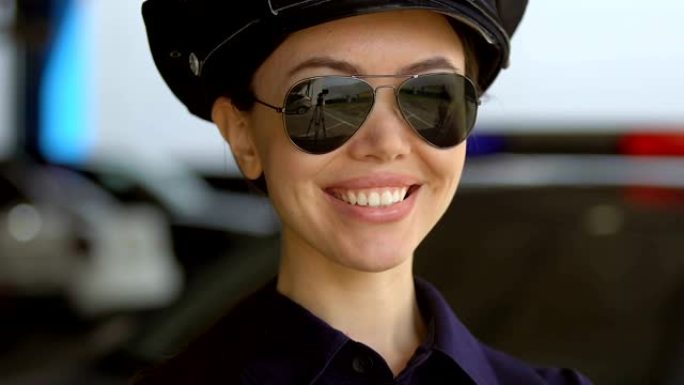 戴着帽子和太阳镜的友好亚洲巡逻女士对相机微笑，保护