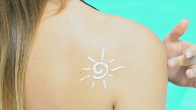 太阳形状的防晒霜在女孩身上的特写镜头，在游泳池附近晒日光浴