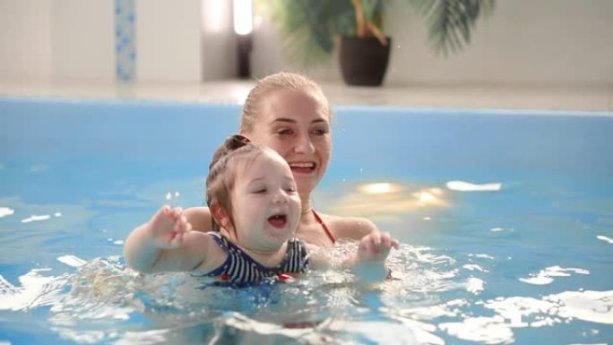 游泳池里的年轻妈妈和她的小女儿在慢动作中玩耍。从事积极生活方式的体育家庭