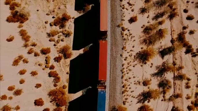 当摄像机低头看着沙漠中经过的集装箱火车时，一架美丽的无人机进行了跟踪。
