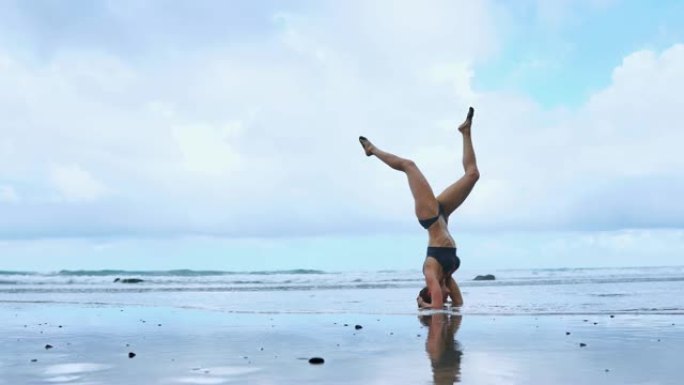 灵活的瑜伽女人向前伸展弯曲触摸前额到膝盖户外日落海滩特写。专业体操运动员健身教练赤脚站在沙滩上表演a