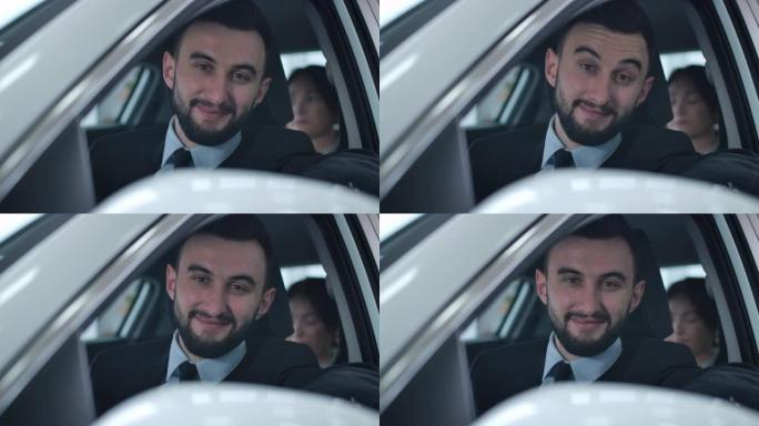 积极的年轻白人男子坐在车里和乘客看着相机的肖像。微笑的专业司机在出租车或私人司机工作。电影院4k P