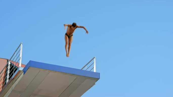 SLO MO男潜水员跳下平台在空中旋转降落在蓝池