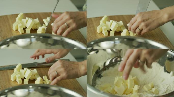一名年轻女子的手用一把大菜刀在木制砧板上将黄油切成小块，捡起黄油，然后将其撒在金属搅拌碗中的面粉上