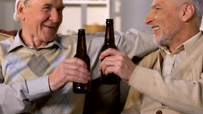老人坐在沙发上喝啤酒，朋友在享受周末时碰杯