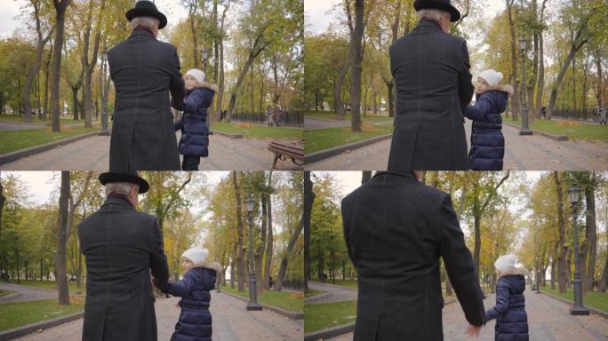 一个穿着优雅的黑色帽子和外套的成熟高加索男人的后视图与他的孙女漫步