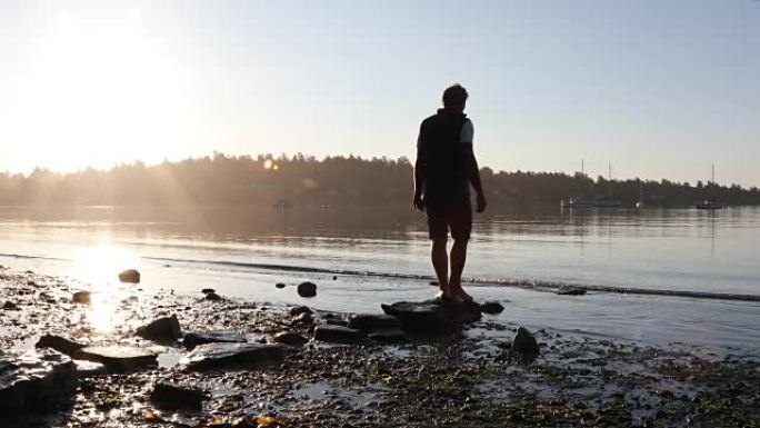 人在日出时在空旷的海滩上沿着垫脚石平衡