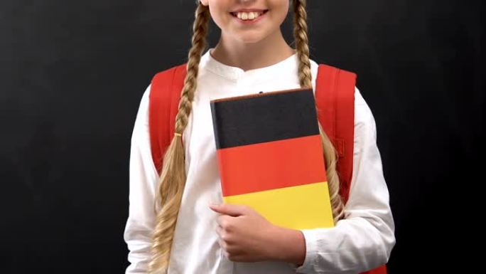 可爱的女学生拿着德国国旗的书，学习语言，教育