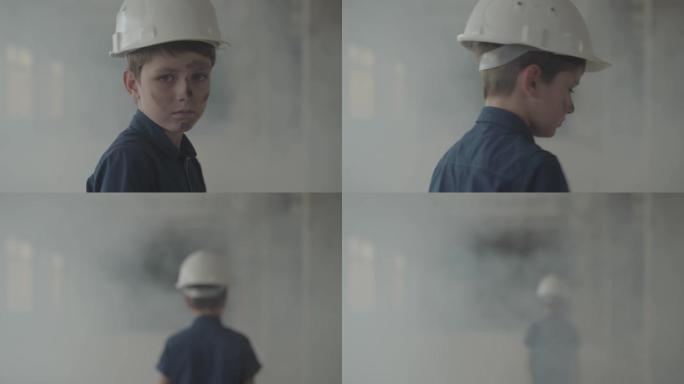 戴着防护头盔的男孩的肖像从烟柱里出来，看着相机。