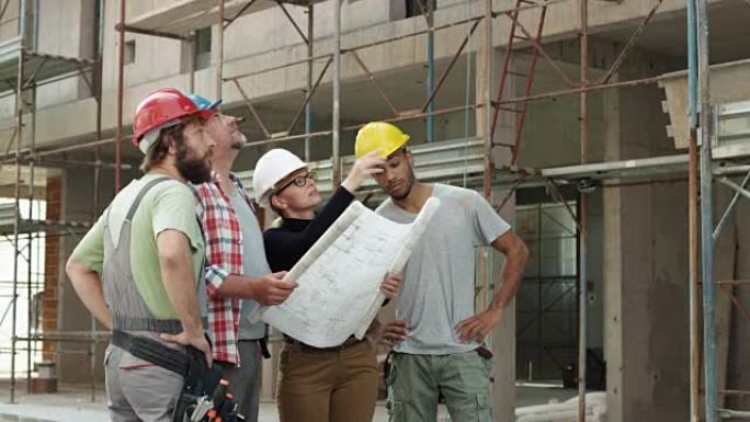 女建筑师，一名工头和两名建筑工人在施工现场看着外面的平面图，并指着建筑物检查进度