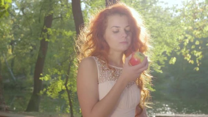 美丽的白衣白人妇女在秋天的公园里吃红苹果。特写视图。