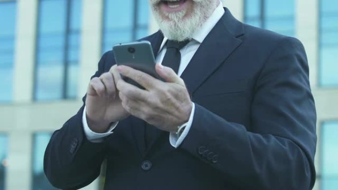 老商人表现出Yes手势，从智能手机上阅读好消息，特写镜头