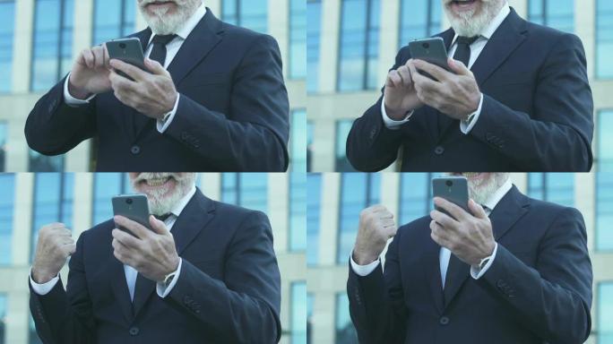 老商人表现出Yes手势，从智能手机上阅读好消息，特写镜头