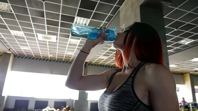 运动中的女性。美丽的红发女人在健身房喝水