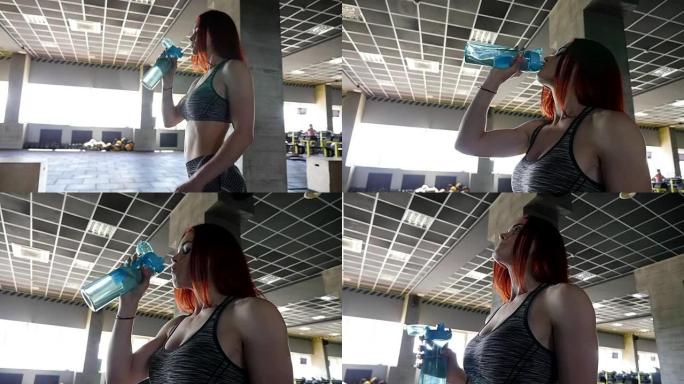 运动中的女性。美丽的红发女人在健身房喝水