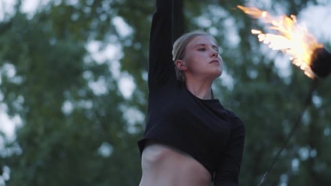 金发自信的女人在森林或公园里站着火焰表演的肖像。