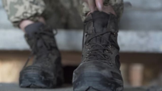 近距离的年轻妇女的手在军事制服系紧她的旧鞋子。