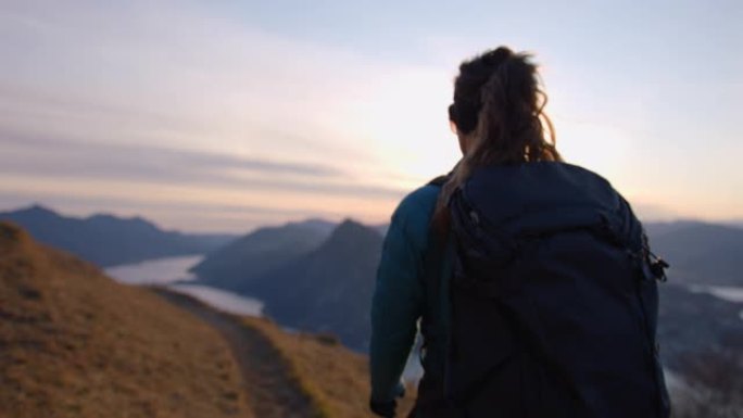 女徒步旅行者登上山路，俯瞰湖泊和日落