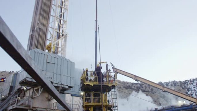 在寒冷的冬天早晨，油田工人在石油和天然气钻井平台现场索具钻杆的慢动作镜头